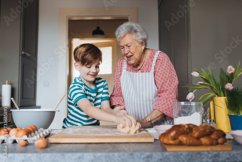 Grandmother with grandson preparing traditional easter meals, kneading dough for easter cross buns. Passing down family recipes, custom and stories.