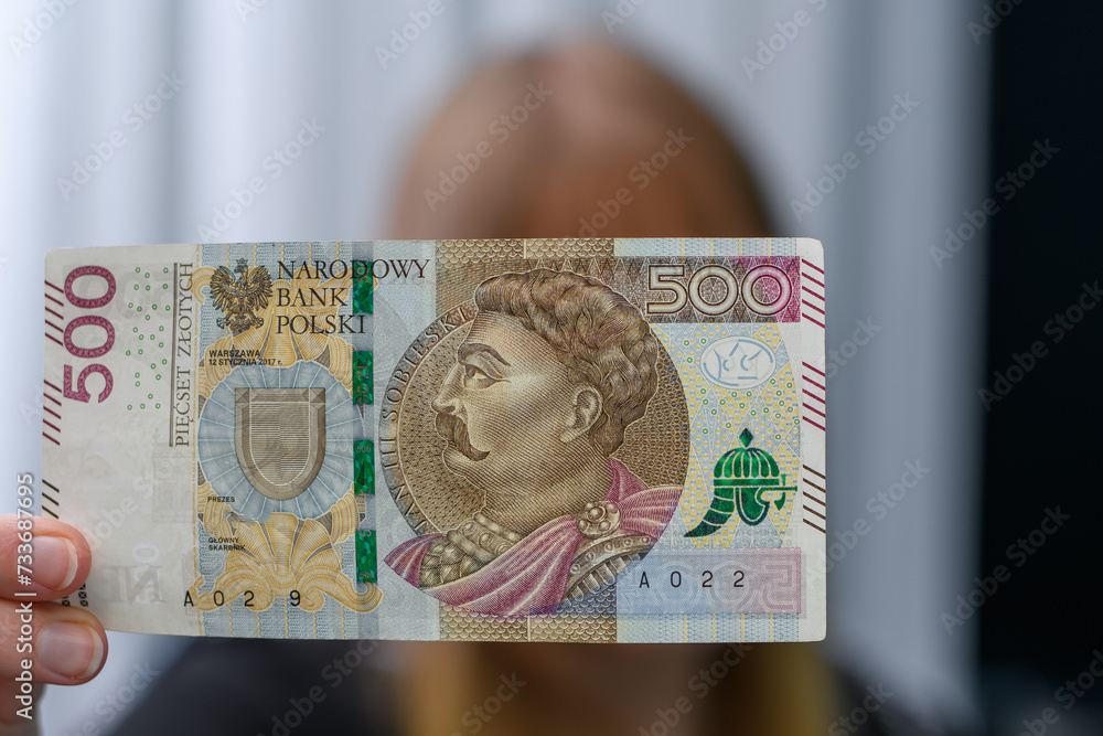 Fototapeta premium Kobieta trzyma w dłoni polski banknot 500zł, sprawdza czy nie jest fałszywy 
