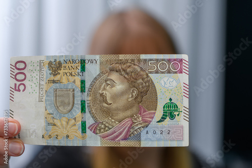 Kobieta trzyma w dłoni polski banknot 500zł, sprawdza czy nie jest fałszywy 