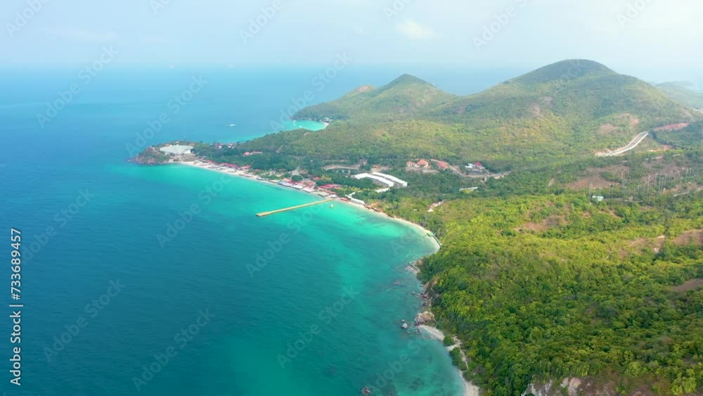 Tropical island with a sandy azure bay and pier and a beach village settlement surrounded with roads by exotic green forests trees hills, aerial view Tropical island with a sandy azure bay and pier and a beach village settlement surrounded with roads by exotic green forests trees hills, aerial view