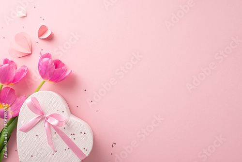 Quintessential girly party layout. Top view of a heart-shaped box with a ribbon, sparkles, love hearts, and a fresh bunch of tulips on a pastel pink backdrop, with space for copy