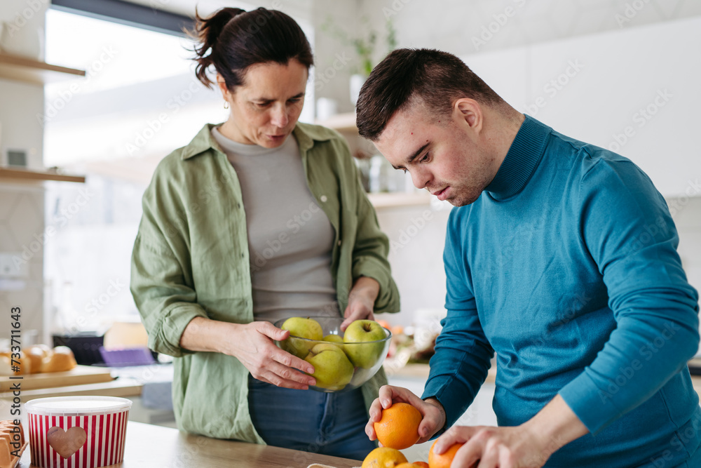 Fototapeta premium Young man with Down syndrome preparing breakfast with his mother at home. Morning routine for man with Down syndrome.