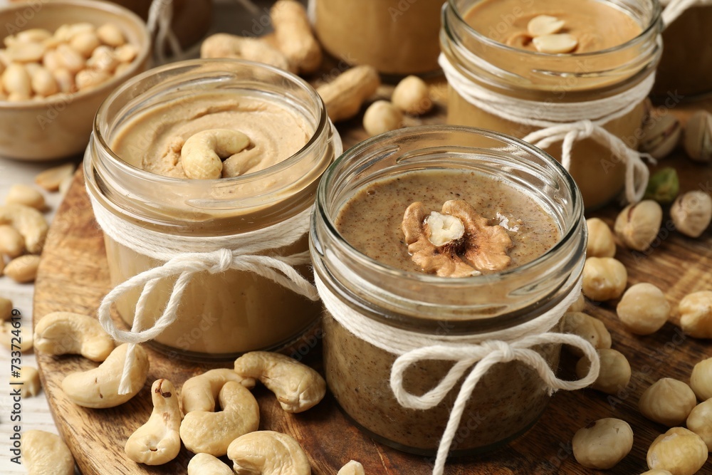 Tasty nut butters in jars and raw nuts on table, closeup Tasty nut butters in jars and raw nuts on table, closeup