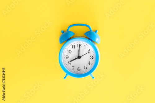 Blue alarm clock on a yellow background, top view.
