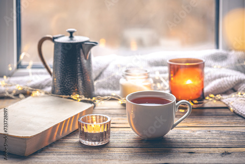 Cozy composition with a cup of tea  a book and candles by the window.