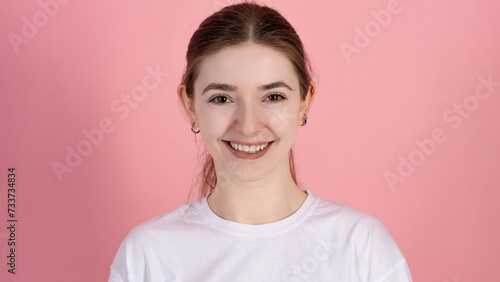 Portrait of a happy attractive Caucasian young brunette woman in casual white t-shirt isolated on pink studio background. Youth, beauty, joy.