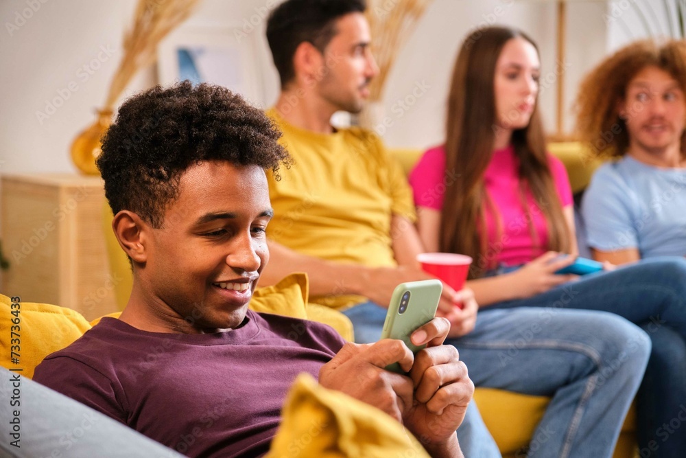 Young smiling Black man using his smartphone laying on the sofa at shared student flat. Young smiling Black man using his smartphone laying on the sofa at shared student flat.