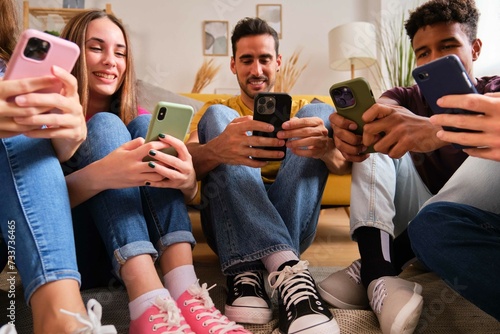 Obraz na płótnie Multiracial friends looking at their mobile phones sitting on a semicircle at a shared students flat. w salonie