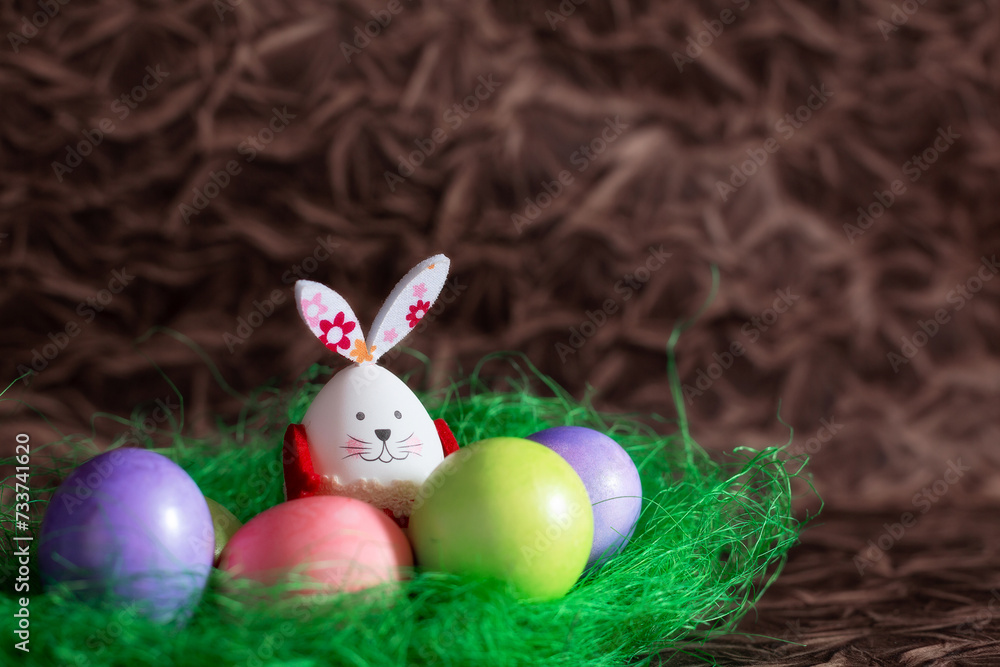 Colorful Easter eggs and bunny rabbit in green next decoration on brown copy space background