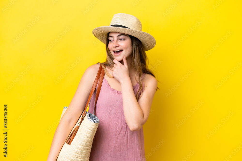 Young caucasian woman holding a beach bag isolated on yellow background looking to the side and smiling Young caucasian woman holding a beach bag isolated on yellow background looking to the side and smiling