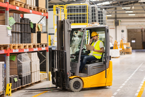 Warehouse forklift driver controlling shipping order. Warehouse worker preparing products for shipmennt, delivery, checking stock in warehouse, order picking.