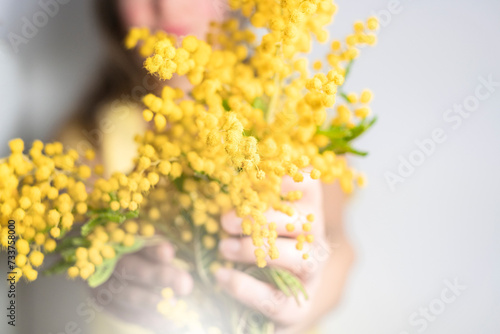 Close up hand of young girl or woman holds yellow brunch of mimosa flowers. 8 march women's day concept. © Anna