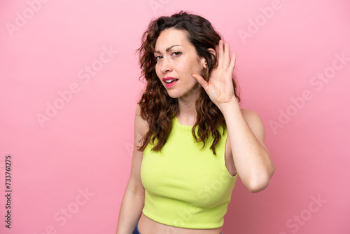 Young caucasian woman isolated on pink background listening to something by putting hand on the ear © luismolinero