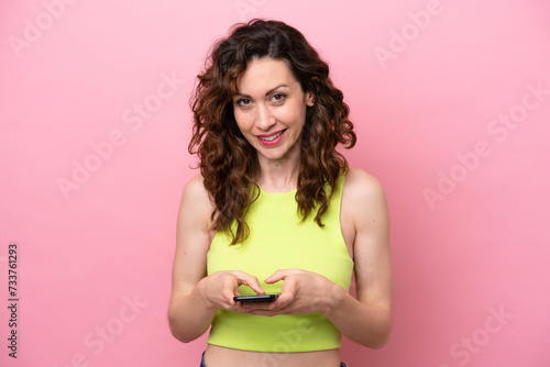 Young caucasian woman isolated on pink background sending a message with the mobile