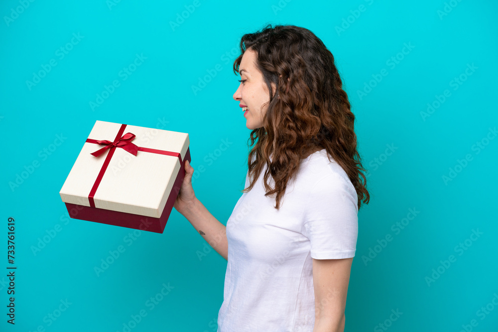 Young caucasian woman holding a gift isolated on blue background with happy expression Young caucasian woman holding a gift isolated on blue background with happy expression