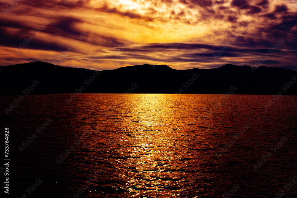 sunset over the lake with the silhouette of the mountains in the background