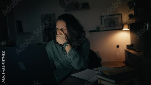 A tired young woman is working on a laptop while sitting in the living room late at night. photo
