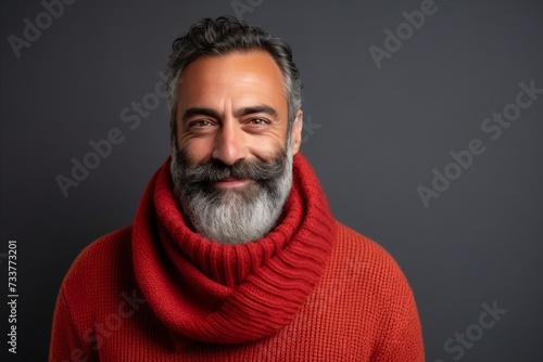 Portrait of a handsome bearded man in red sweater and scarf against grey background