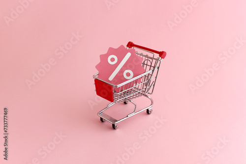Shopping cart with promotional discount sale icon on pink background - banner image for retail promotion, ecommerce, online sales, coupons and specials with space for text photo