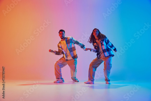 Hip-hop rhythm. Male and female dancers dancing in duet in neon light against gradient studio background. Motion. Concept of movement, energy, dance battles. Dynamic gel portrait © Lustre