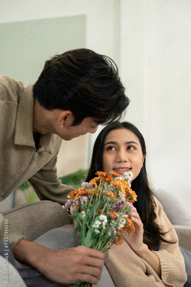 Romantic young asian couple embracing with holding flowers and smiling in living room at home. fall in love. Valentine concept Romantic young asian couple embracing with holding flowers and smiling in living room at home. fall in love. Valentine concept
