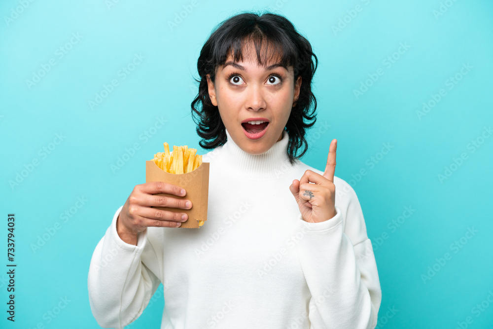 Young Argentinian woman holding fried chips isolated on blue background thinking an idea pointing the finger up Young Argentinian woman holding fried chips isolated on blue background thinking an idea pointing the finger up