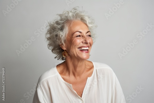 Cheerful senior woman laughing and looking away over grey background.