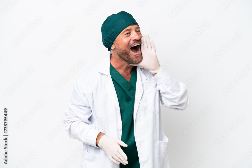 Middle age surgeon in green uniform isolated on white background shouting with mouth wide open to the lateral Middle age surgeon in green uniform isolated on white background shouting with mouth wide open to the lateral