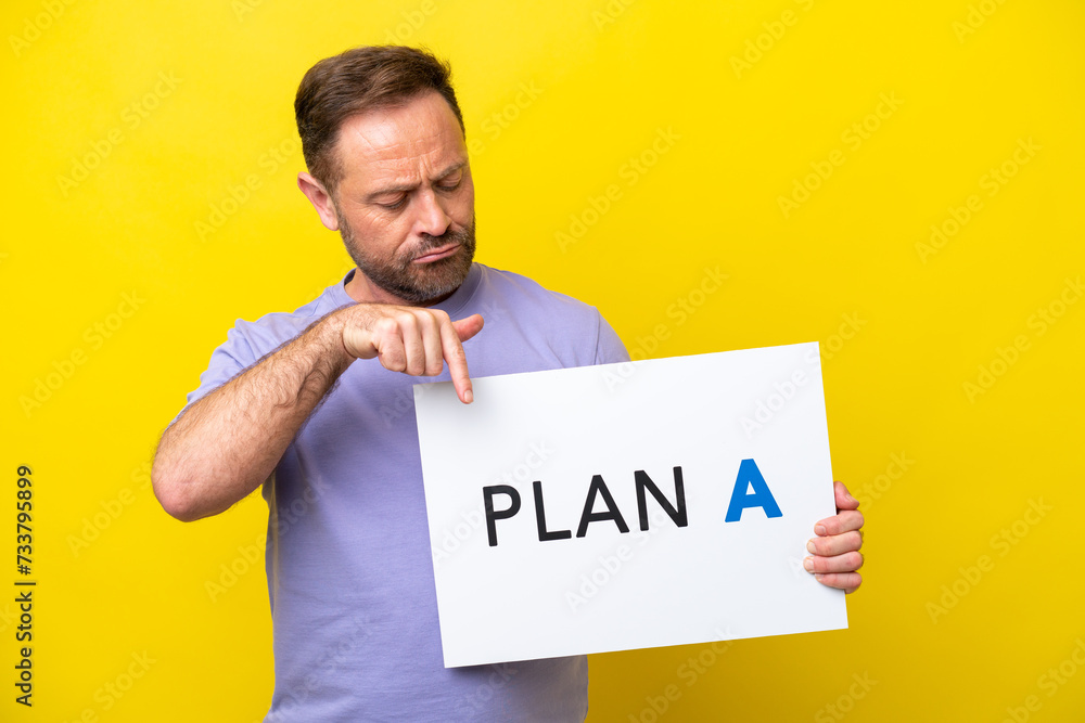 Middle age caucasian man isolated on yellow background holding a placard with the message PLAN A and pointing it Middle age caucasian man isolated on yellow background holding a placard with the message PLAN A and pointing it