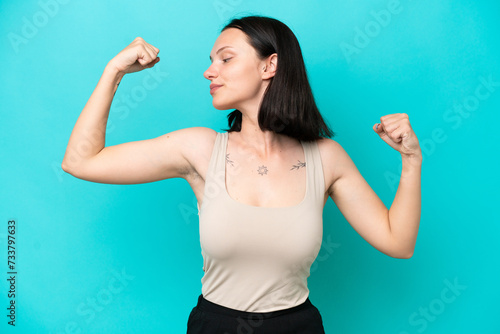 Young caucasian woman isolated on blue background doing strong gesture