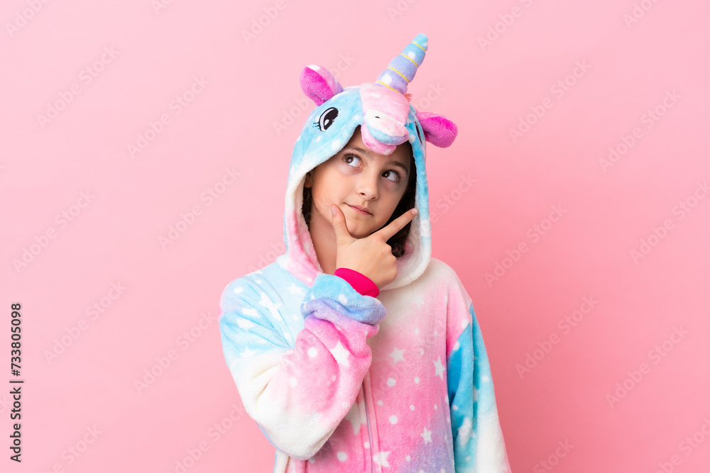 Little caucasian woman wearing a unicorn pajama isolated on pink background having doubts Little caucasian woman wearing a unicorn pajama isolated on pink background having doubts