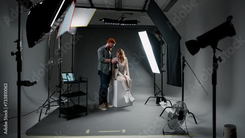 Bearded man making pictures of female model against black background and octabox in professional studio photo