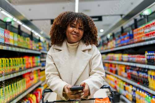 Canvas Print A portrait of beautiful black woman with curly hair with shopping cart in front of her in grocery store