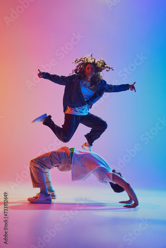 Fototapeta Naklejka Na Ścianę i Meble -  Acrobatic dance pair, woman jumping and man in handstand, against gradient studio background in neon light, filter. Concept of youth culture, music, lifestyle, style and fashion, action. Gel portrait.