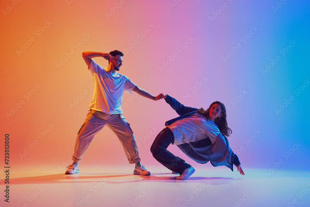 dynamic portrait of man and woman dancing in pair in motion against gradient studio background in neon light, filter. Performance. Concept of youth culture, music, lifestyle, action. Gel portrait.