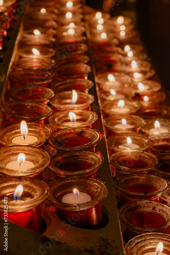Detail of a metal candle stand in a Catholic cathedral. Small devotional lighted candles in small jars represent the petitions of the parishioners. Candles placed on a special candle holder.