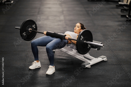 A strong sportswoman is doing workouts with barbell for core and abs in a gum.