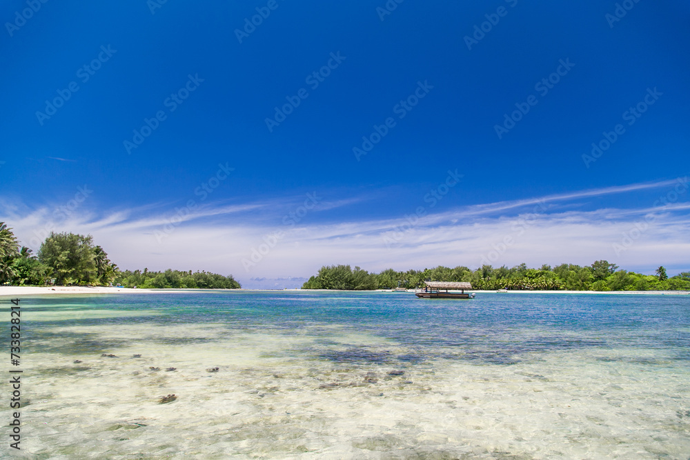 Tropical bay, paradise destination on the Cook Islands. Rarotonga coast during a sunny day. One boat on the sea. Blue sky with clouds. Partly cloudy. Palm trees in distance.