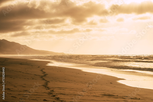 Awesome footprint and sun light beautiful  nature landscape on the coastline and sandy beach with mountains in background and clouds and horizon - summer oudor wild concept and explore lifestyle