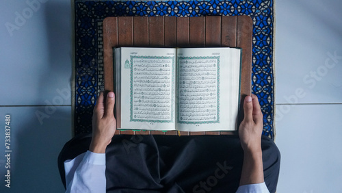 Top view of a Muslim man reading the Quran on a prayer mat