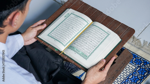close up photo of a Muslim man reading the Quran on a prayer mat during the holy month of Ramadan.