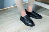 Collection of women's shoes. Black leather sneakers on women's feet. Female feet in comfortable casual sandals