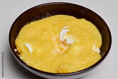(Mamaliga) with cheese, eggs, and cream in a plate.