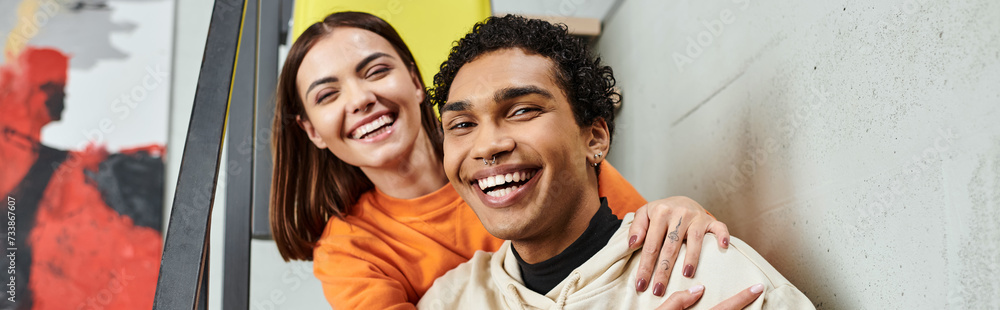 cheerful diverse couple sitting on stairs and smiling during their trip, hostel room, banner cheerful diverse couple sitting on stairs and smiling during their trip, hostel room, banner