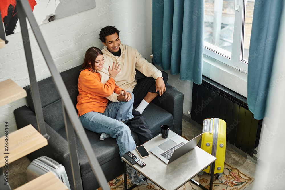 Young multiethnic couple enjoying a quiet moment on a cozy sofa with a laptop in a modern hostel