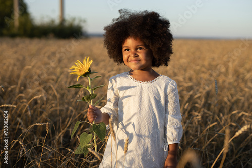 happy african girl with voluminous hairstyle in a field on a walk with a sunflower