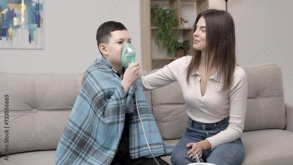 Young woman helping illness boy with nebulizer inhalation at home. A young mother helping her son to inhale with a nebulizer at home Young woman helping illness boy with nebulizer inhalation at home. A young mother helping her son to inhale with a nebulizer at home