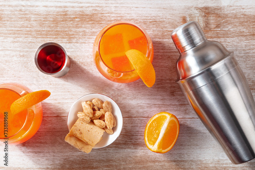 Orange cocktails with a jigger of campari, salty snacks, and a shaker, overhead flat lay shot on a wooden background