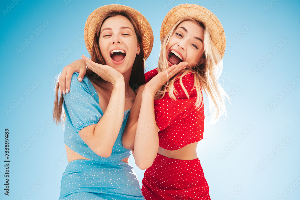 Two young beautiful smiling hipster woman in trendy summer same clothes. Carefree women in street in hats. Positive models at sunset. Cheerful and happy. Bottom view. They look at camera from above Two young beautiful smiling hipster woman in trendy summer same clothes. Carefree women in street in hats. Positive models at sunset. Cheerful and happy. Bottom view. They look at camera from above