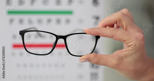Person confidently holds glasses in front of eye test chart photo